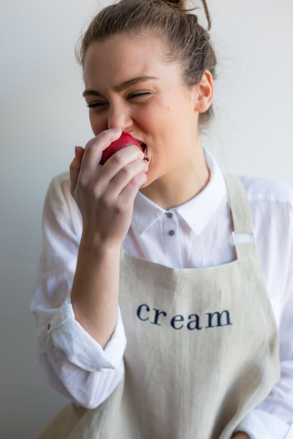 Woman in linen apron biting an apple